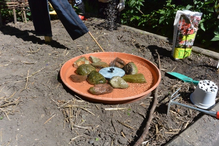 Unser Solarbrunnen schwimmt in einem Blumenuntersetzer. Er wird von faustgroßen Steinen in der Mitte des Untersetzers gehalten, damit das Wasser immer wieder in die Schale läuft und neu hochsprudeln kann.