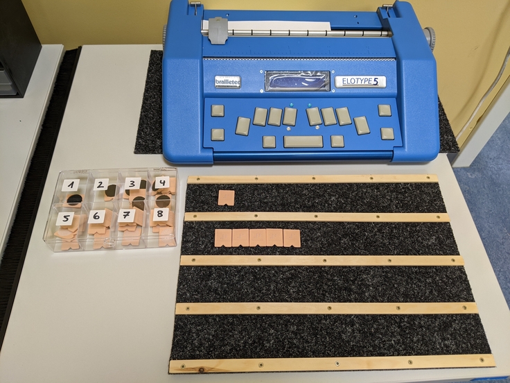 Eine Schreibmaschine für Blindenschrift eine EloType 5, Plättchen und eine Unterlage für die Plättchen.