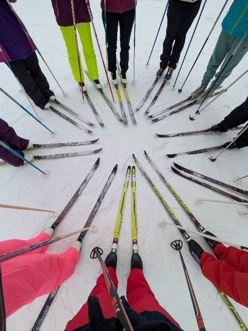 Mehrere Personen stehen mit Skiern in einem Kreis und jemand hat ein Foto von oben, von den Skiern gemacht.