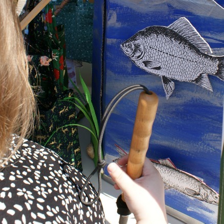 eine Frau vor einem Bild mit einem blauen Fisch und sie hat einen Langstock in der Hand.