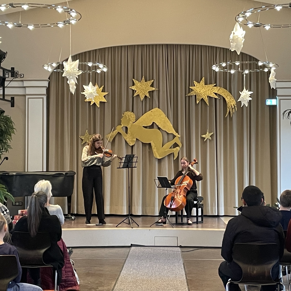 Schülerinnen und Schüler sitzen in der Aula und hören den beiden Musikerinnen aufmerksam zu.